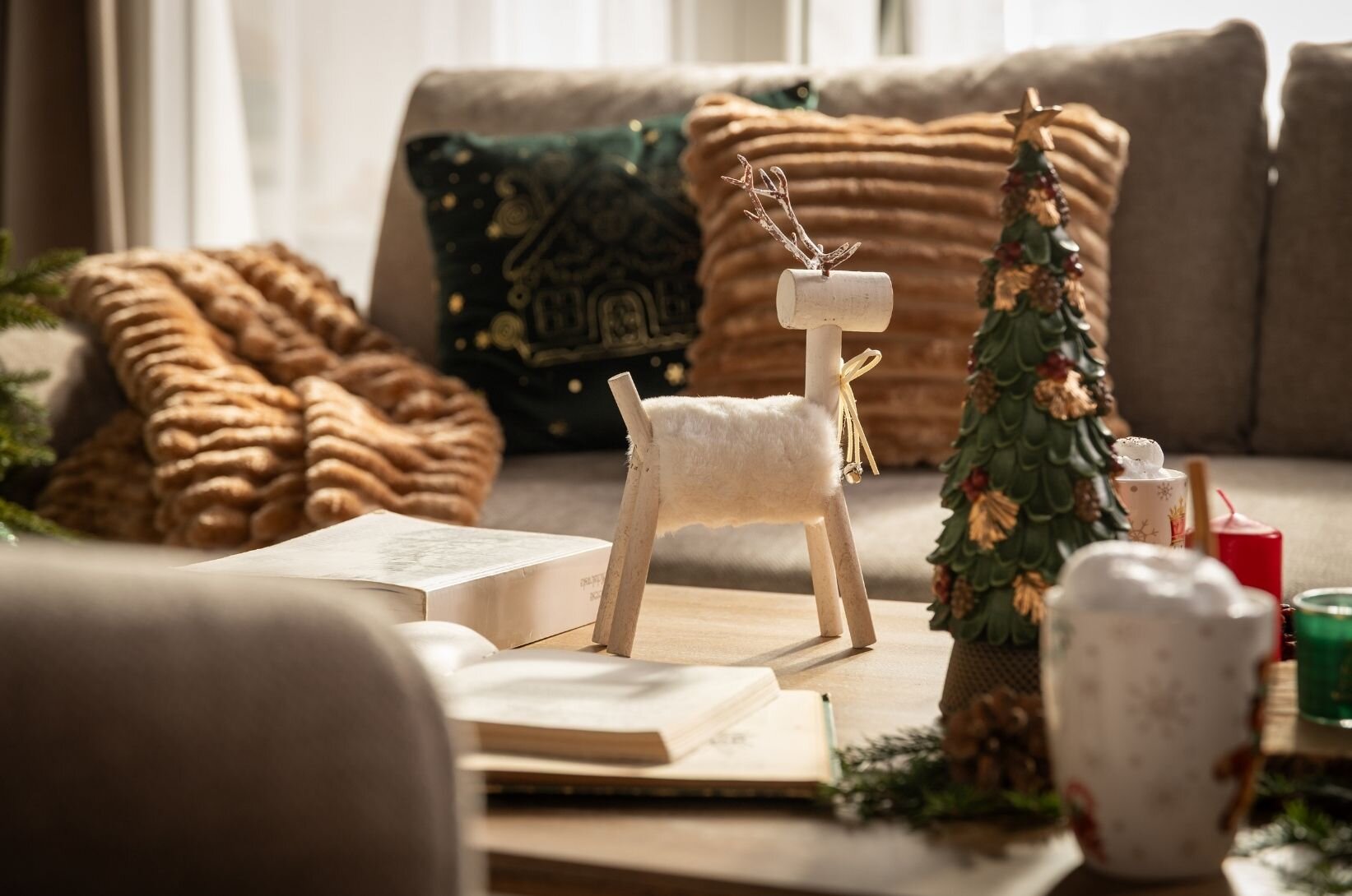Dekorace v obývacím pokoji: vánoční figurka, hrnek, deka a dekorativní polštáře.