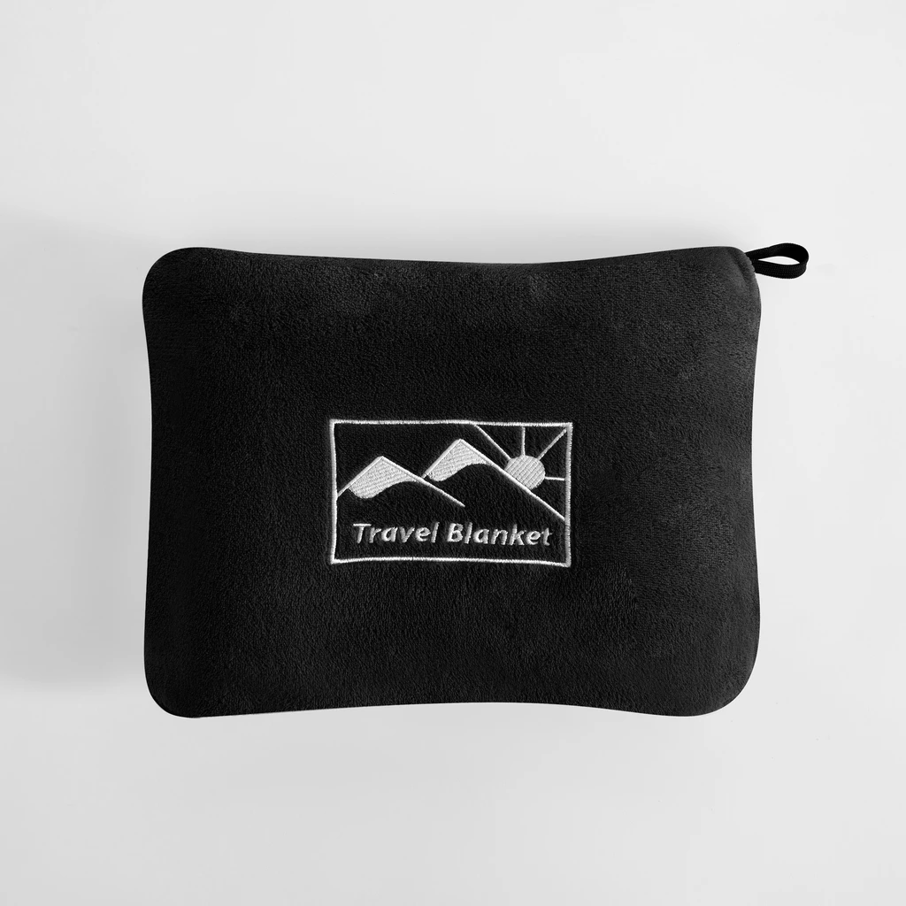 Czarny koc podróżny złożony do pokrowca o tym samym kolorze. Na pokrowcu logo przedstawiające słońce wychodzące zza gór oraz napis Travel Blanket. U jednego z rogów pokrowca pętelka-uchwyt.