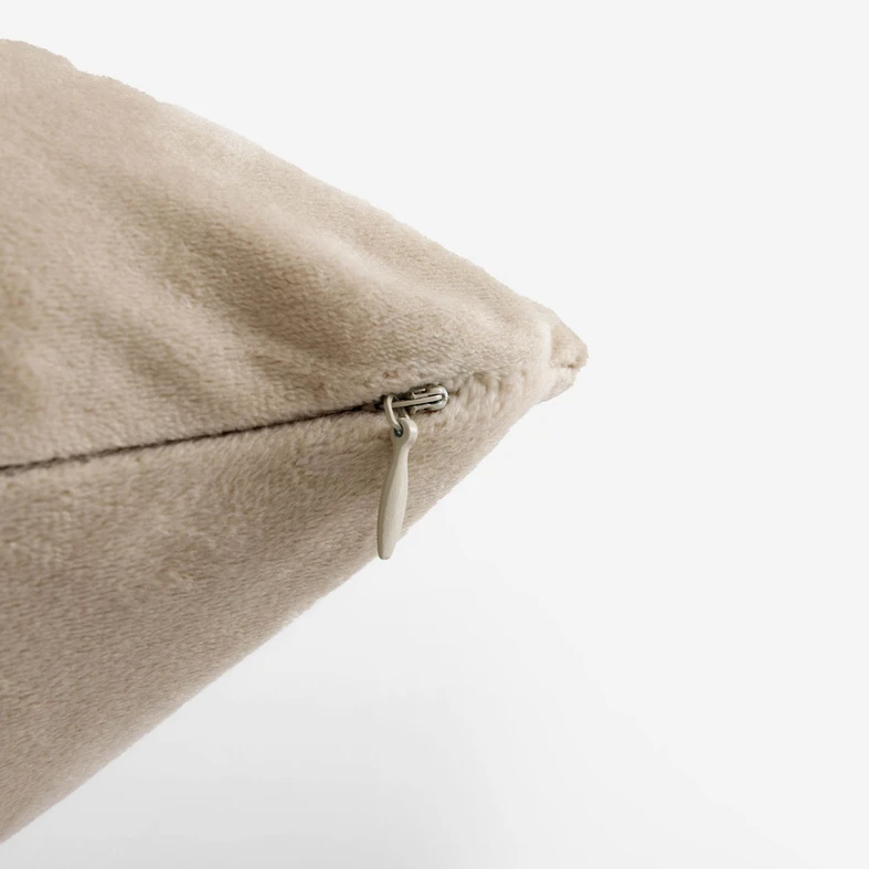 Zbliżenie na róg beżowej poszewki i uchwyt zamka w tym samym kolorze. 