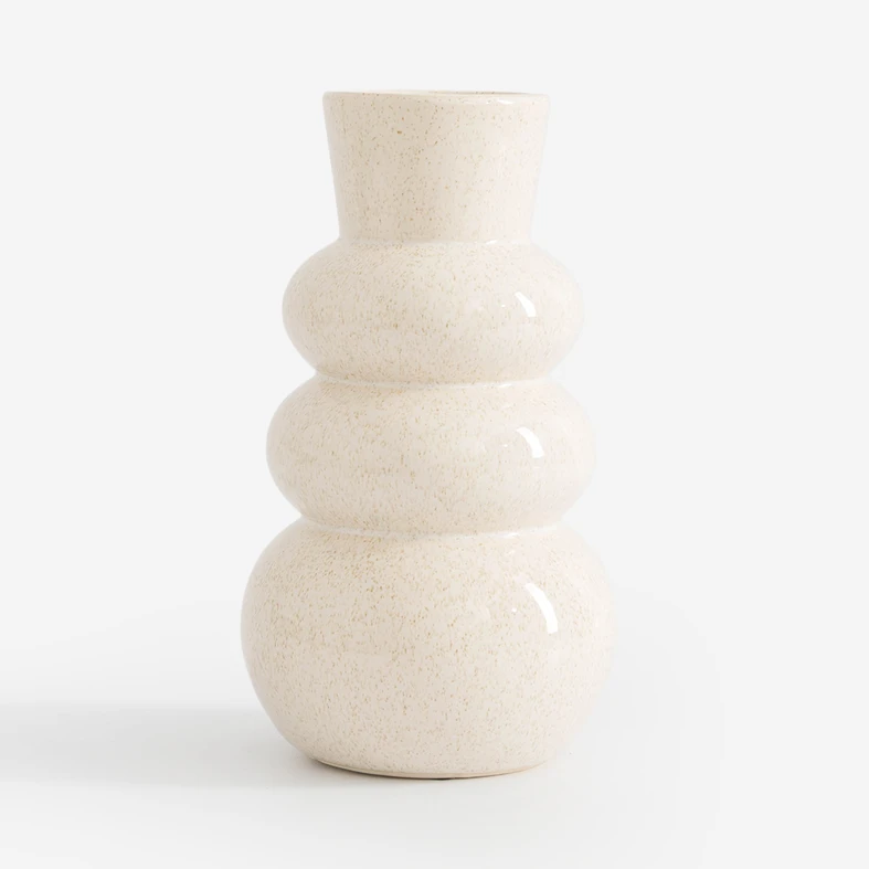 Ceramiczny wazon w kolorze kremowym. Obłości przypominają sylwetkę bałwanka. Nakrapiany drobnymi jasnobrązowymi piegami.