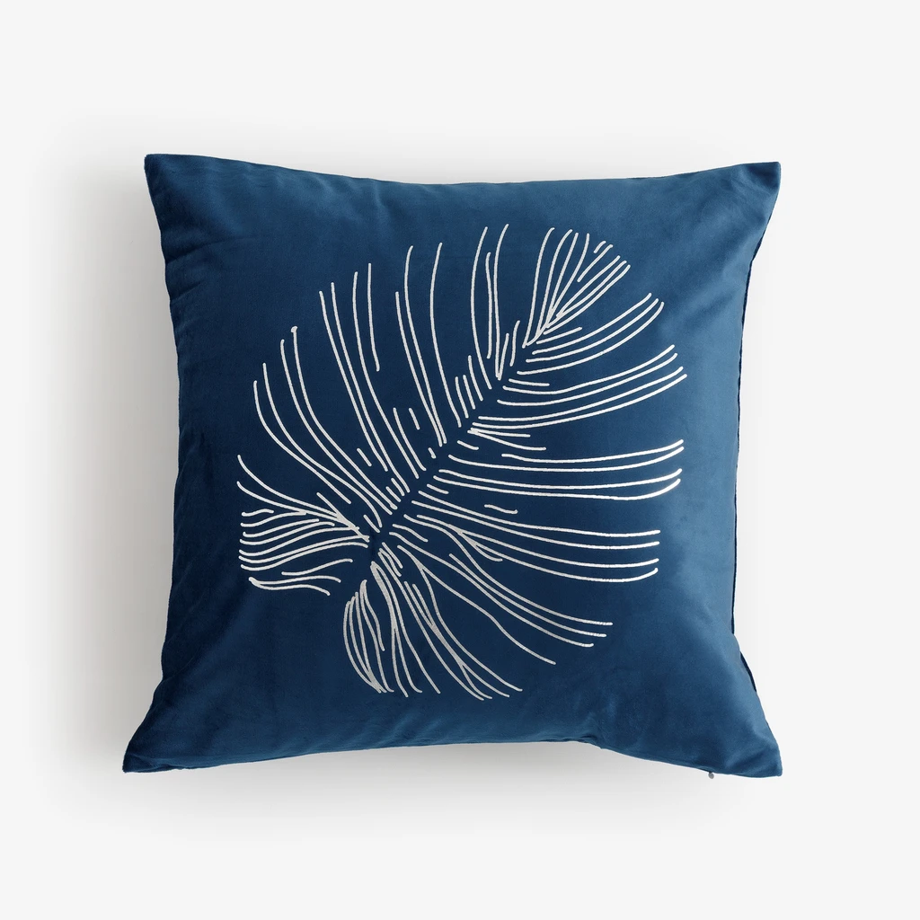 Ciemnoniebieska, kwadratowa poszewka dekoracyjna z poliestru przypominającego welur, ze srebrnym nadrukiem liścia monstery. 