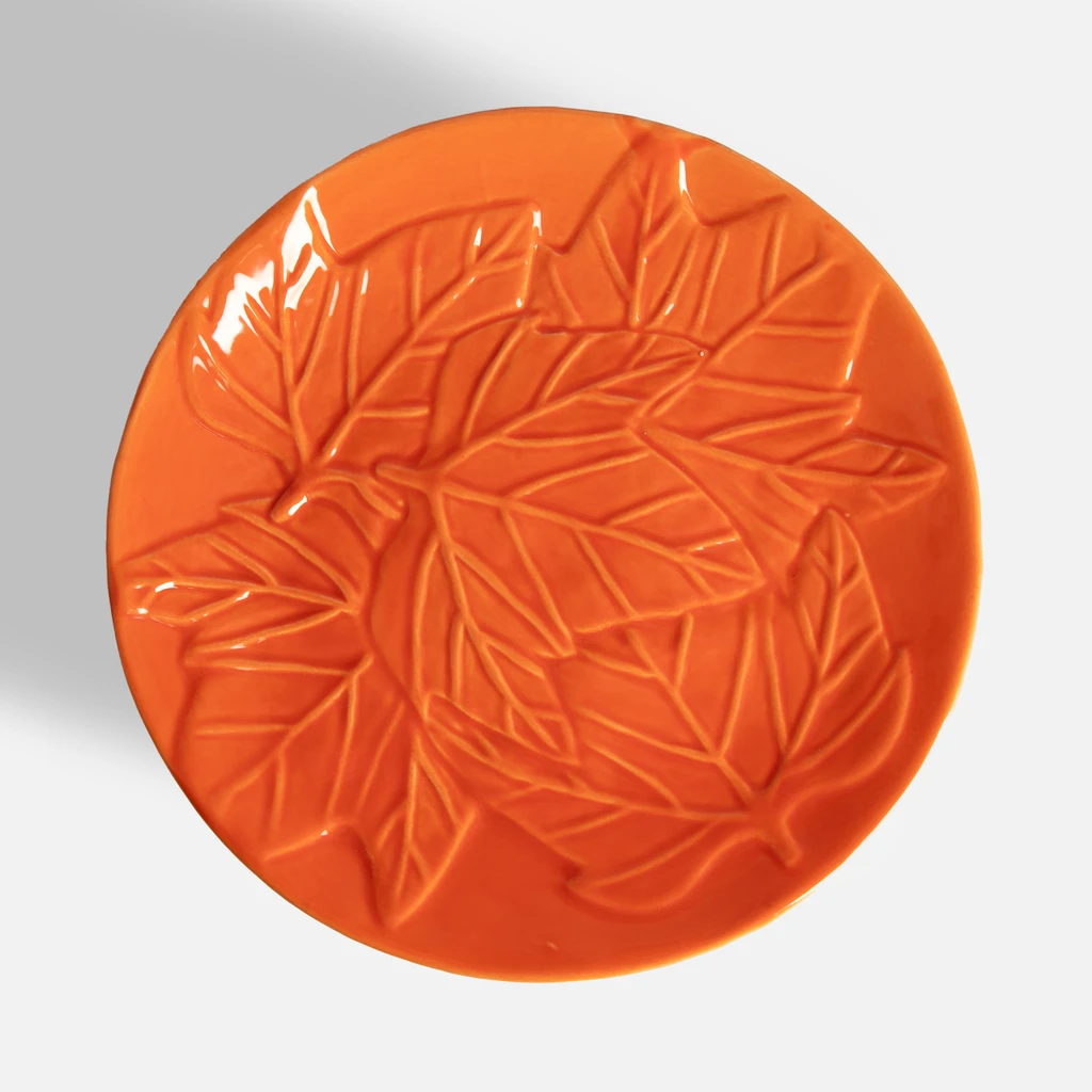 Pomarańczowa patera na nóżce, z dekoracyjnym wzorem liści na powierzchni, widok z góry.