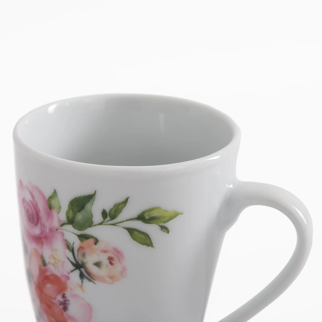 Detal kubka, kwiatowy wzór na białej porcelanie. Różowo-koralowe róże i zielone listki.