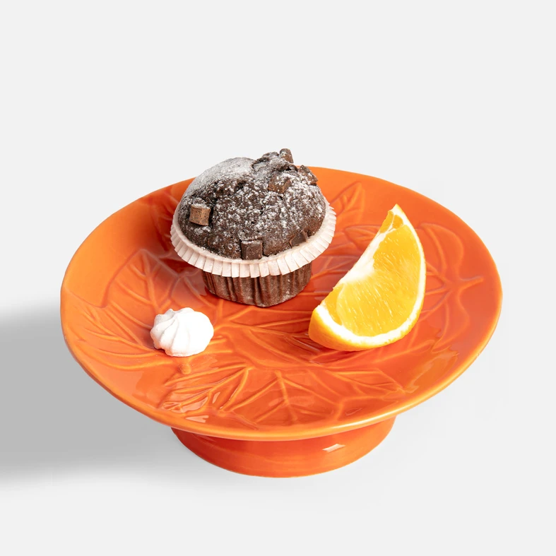 Patera z widocznym deserem: czekoladowy muffin, plaster pomarańczy i bezy na pomarańczowym talerzu z liśćmi.