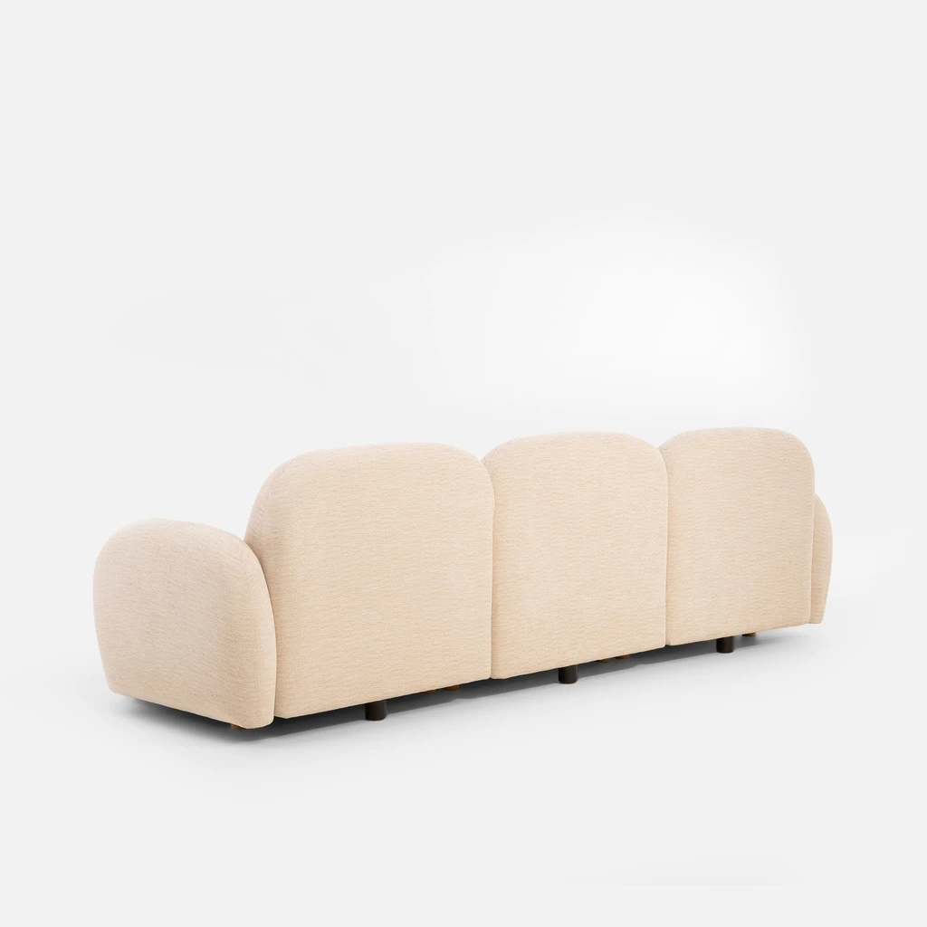 Tył beżowej sofy z widocznymi zaokrągleniami i jednym podłokietnikiem