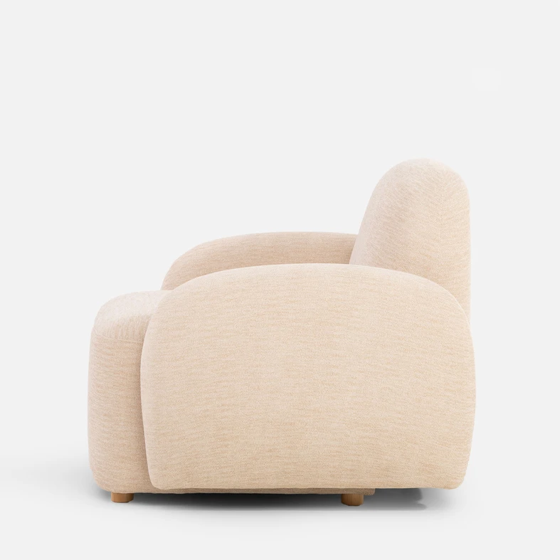 Beżowy fotel o obłych kształtach, z niskimi nóżkami z jasnego drewna - widok od boku