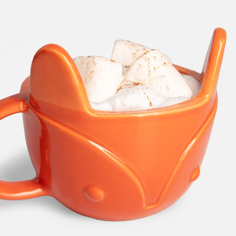 Zbliżenie na kubek w kształcie lisa. Wypełniony jest napojem z bitą śmietaną i piankami marshmallow.