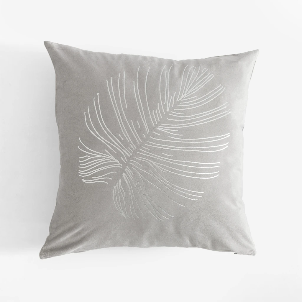 Jasnoszara, kwadratowa poszewka dekoracyjna z poliestru przypominającego welur, ze srebrnym nadrukiem liścia monstery. 